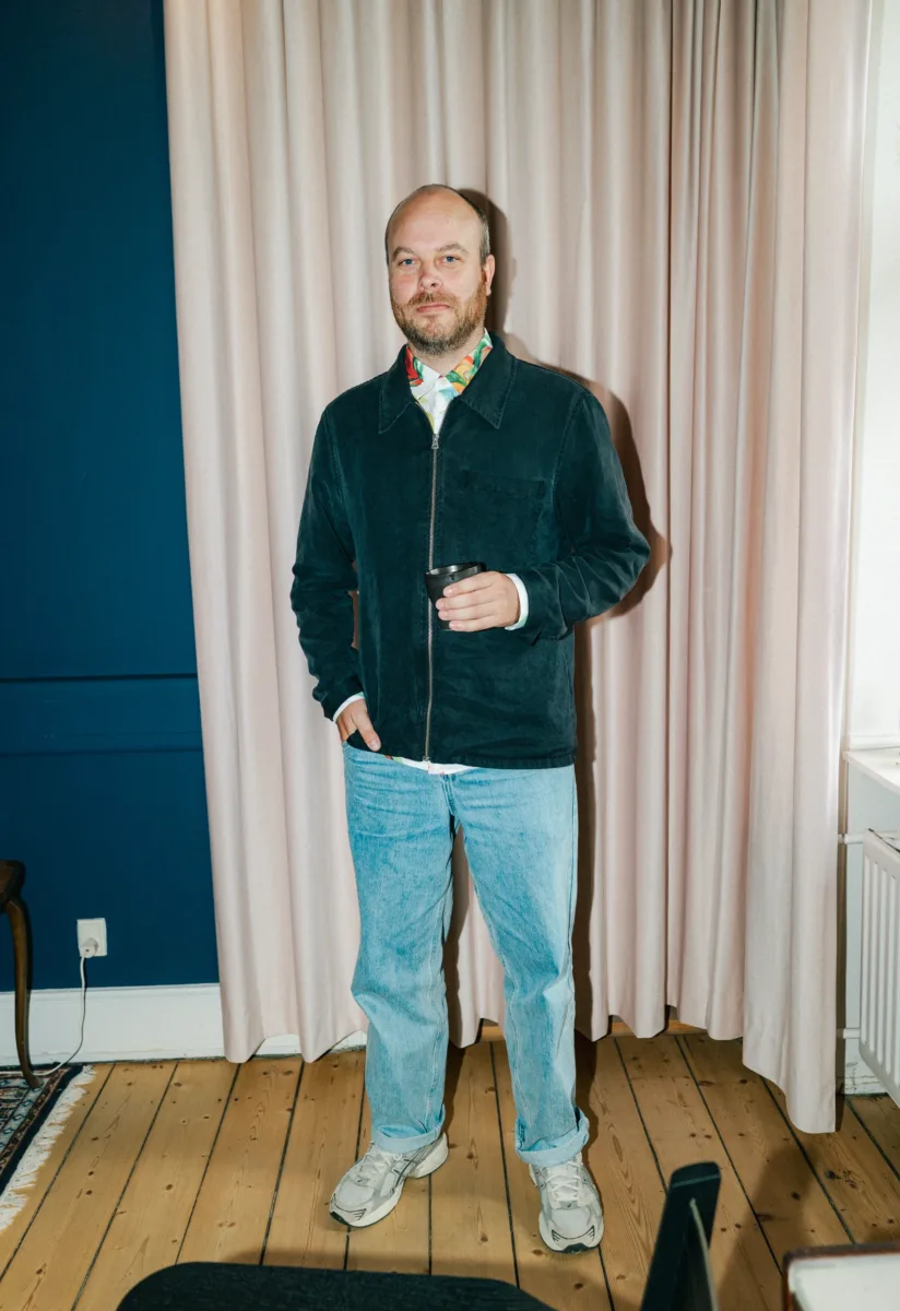 Medarbejder står med en sort kop i hånden foran et lyst gardin i et blåt lokale