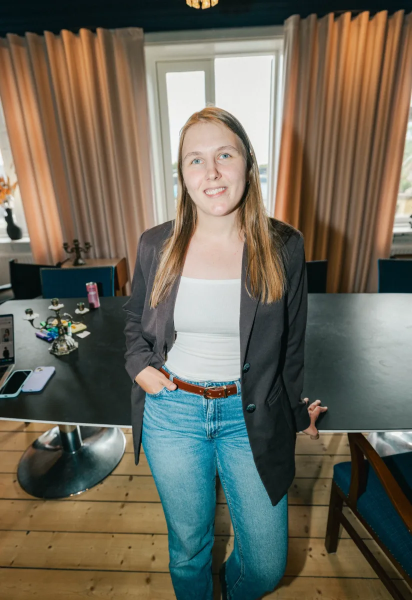 Medarbejder står ved et mødebord med telefon og bærbar computer foran lyse gardiner