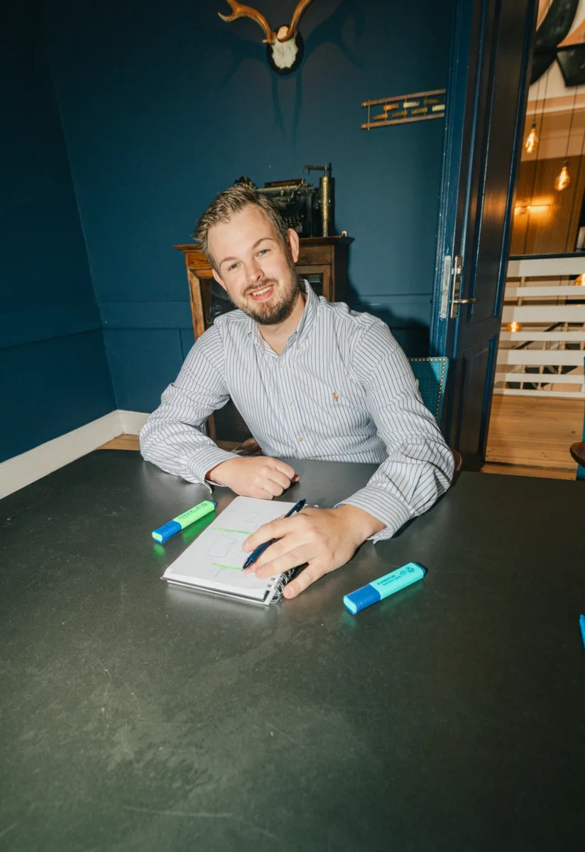 Medarbejder sidder ved et mødebord med notesblok, kuglepen og to markers