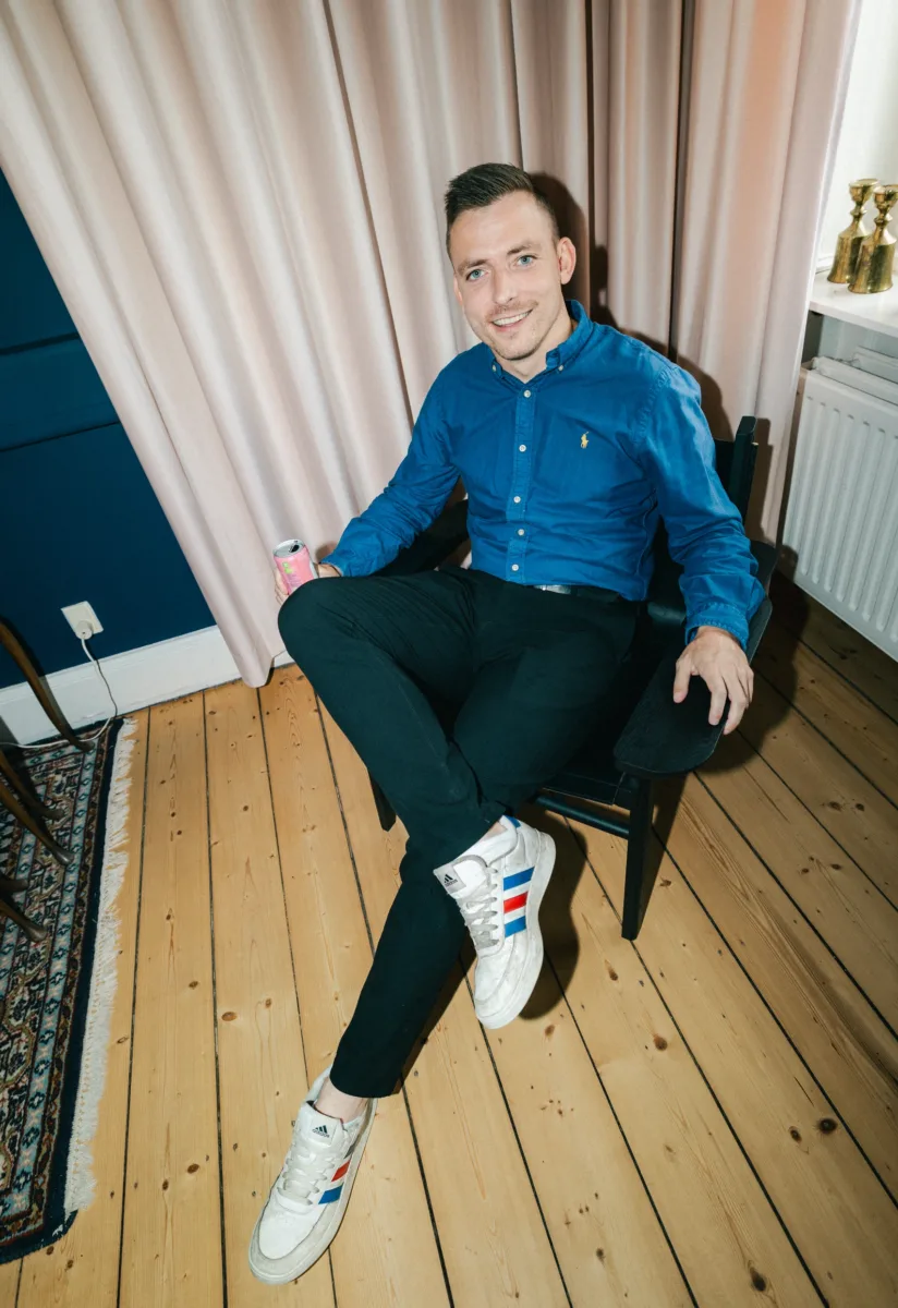Medarbejder i blå skjorte sidder med en dåse foran et lyst gardin