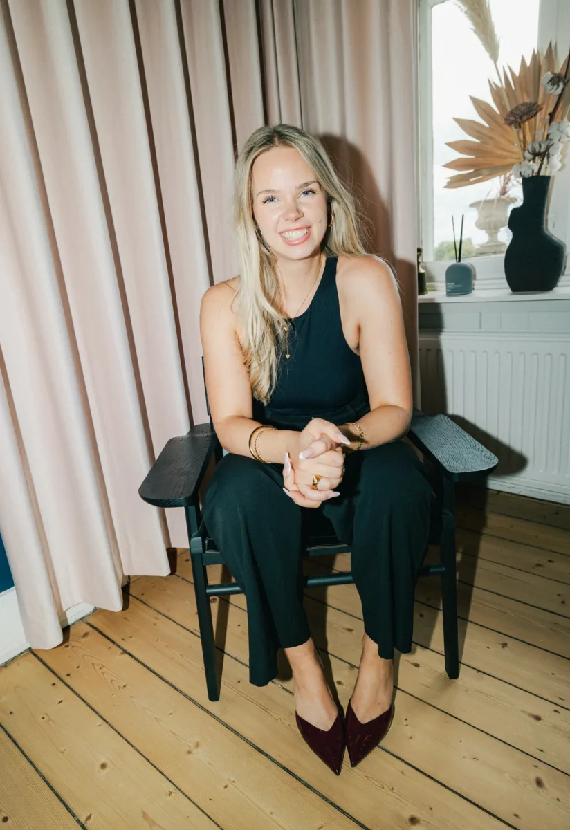 Medarbejder sidder smilende med foldede hænder i en sort lænestol