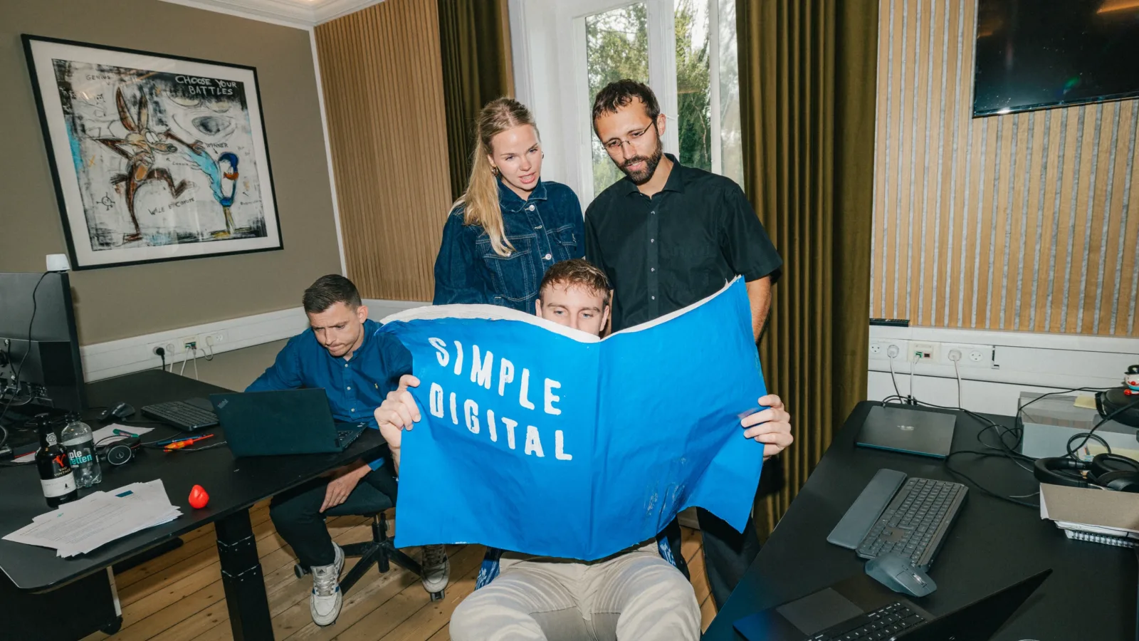 Tre kolleger kigger sammen i en stor blå plakat med teksten Simple Digital