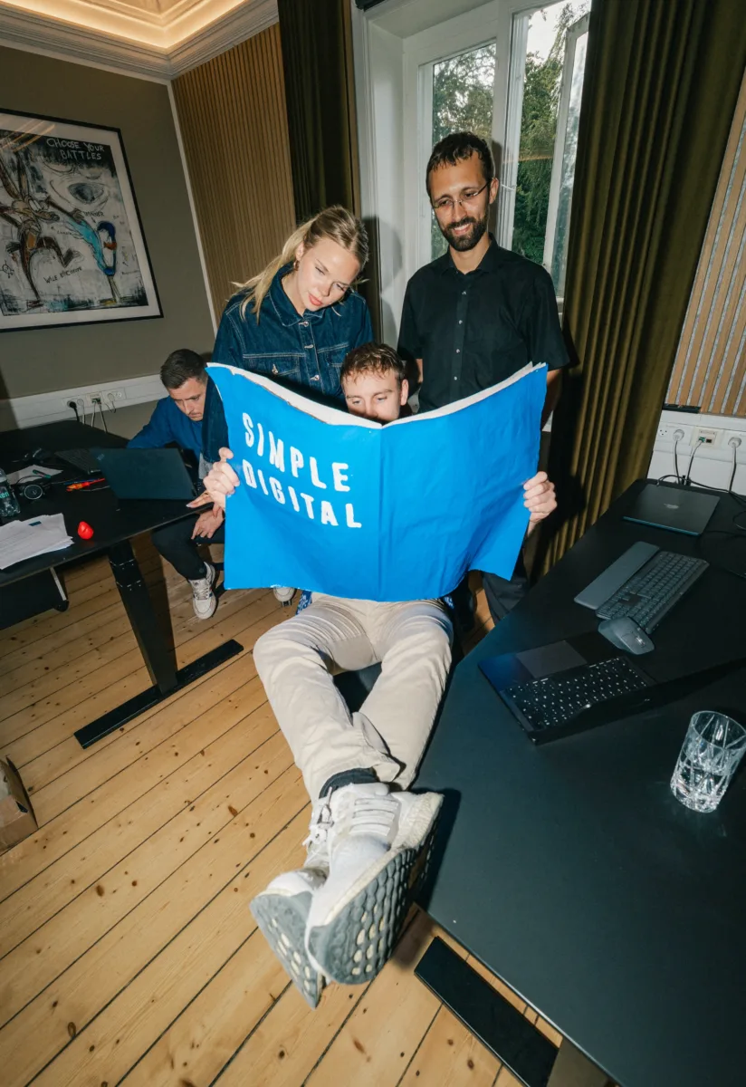 Kolleger studerer en blå plakat med teksten Simple Digital på et åbent kontor