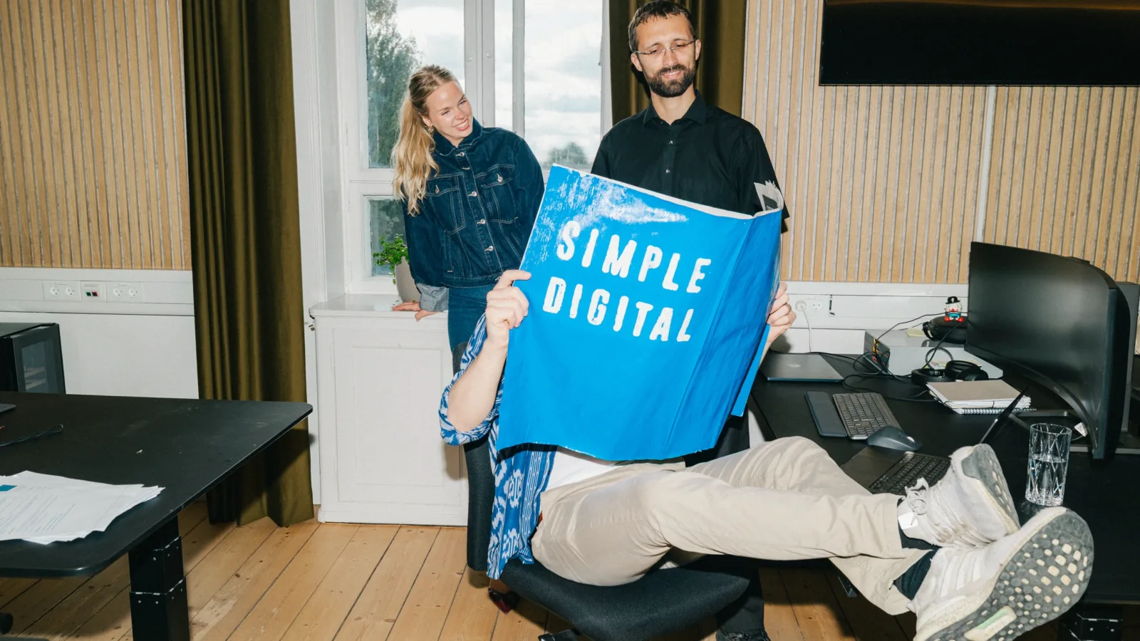 Medarbejder holder en Simple Digital-plakat op med benene oppe på skrivebordet
