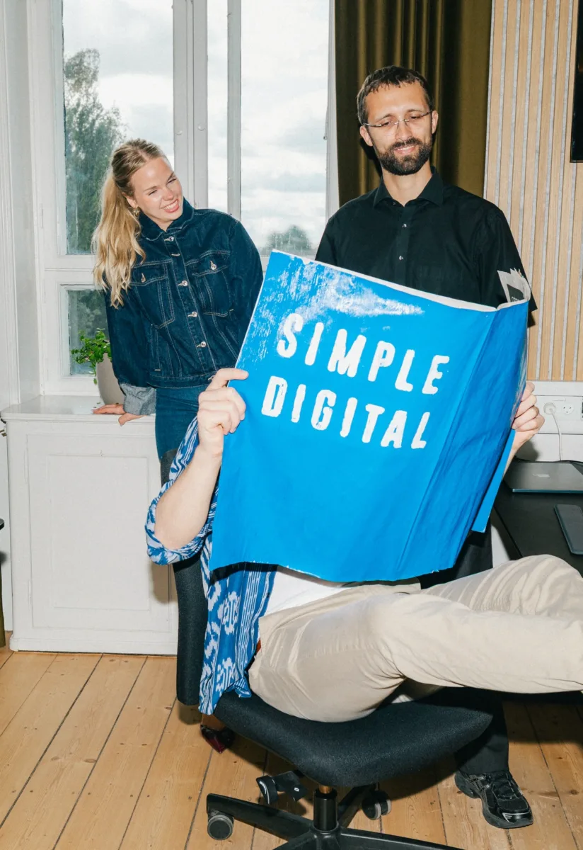 Medarbejder holder en Simple Digital-plakat op med benene oppe på skrivebordet