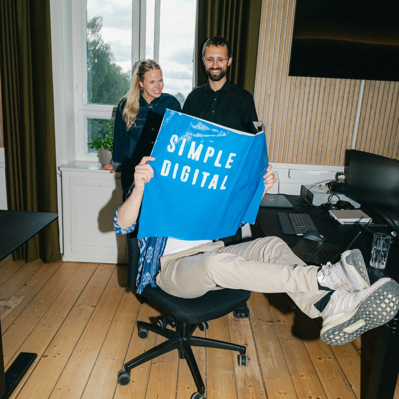 Kolleger griner sammen om en blå plakat med teksten Simple Digital