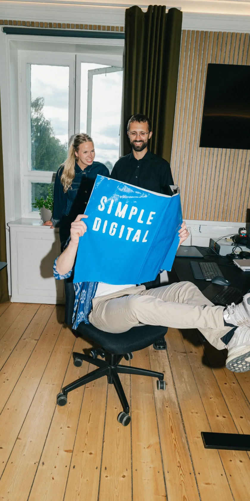 Kolleger griner sammen om en blå plakat med teksten Simple Digital