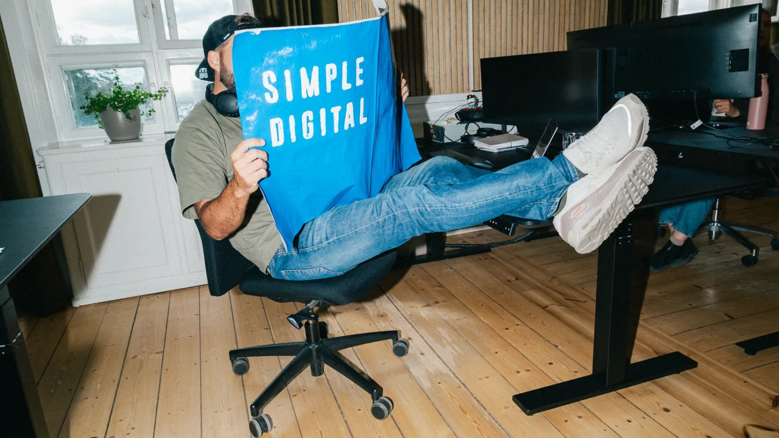 Medarbejder med kasket holder en blå Simple Digital-plakat foran ansigtet
