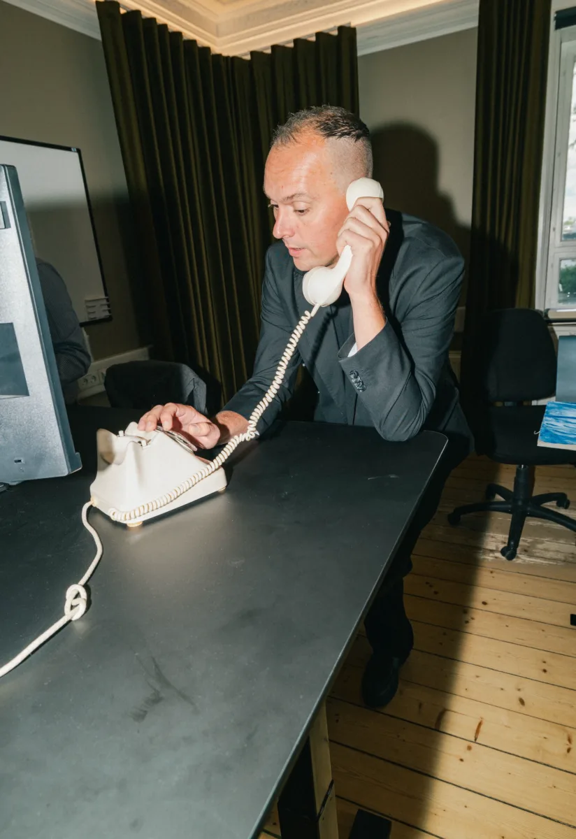 Medarbejder taler i en gammel drejeskivetelefon lænet ind over et skrivebord