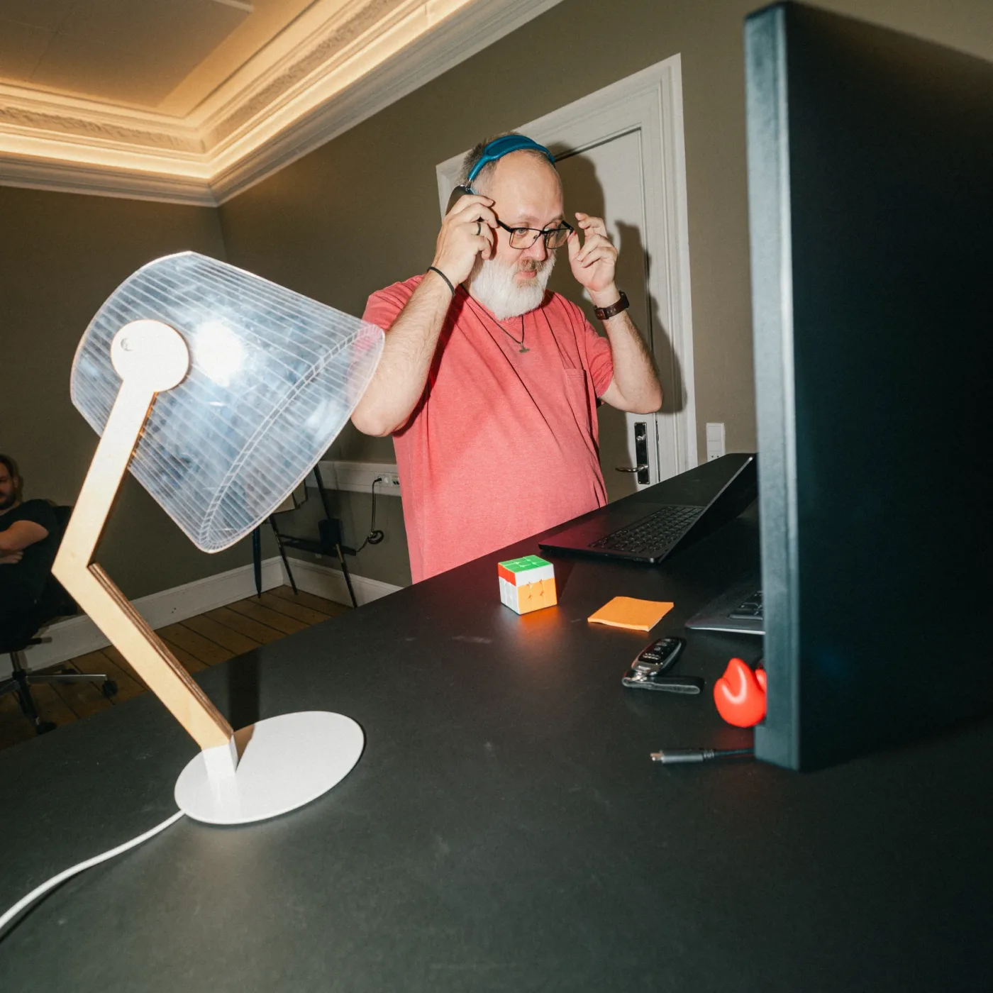 Medarbejder tager hovedtelefonerne af ved et skrivebord med bordlampe