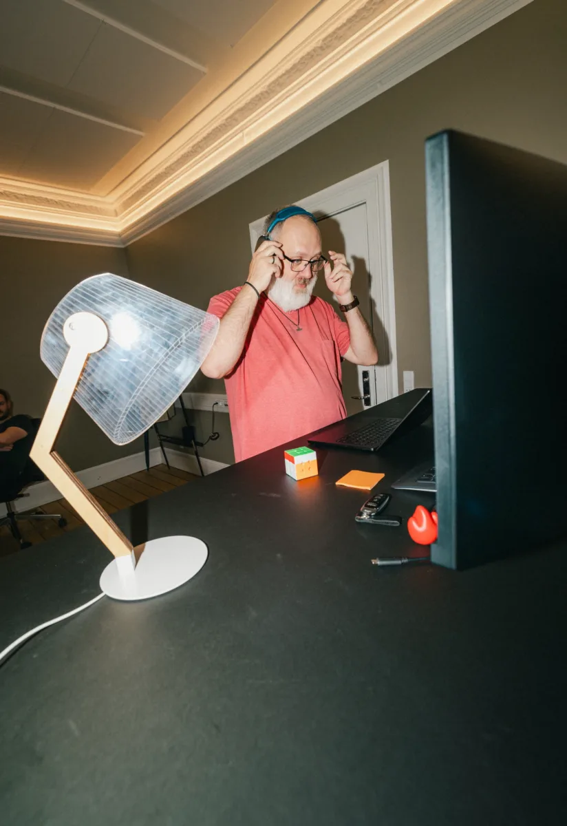 Medarbejder tager hovedtelefonerne af ved et skrivebord med bordlampe