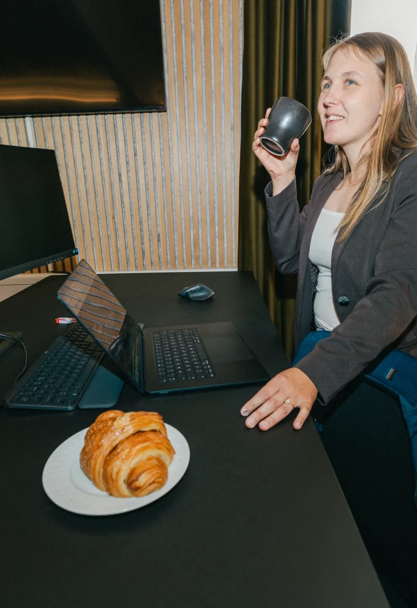 Medarbejder drikker kaffe ved sin arbejdsplads med bærbar computer og skærm