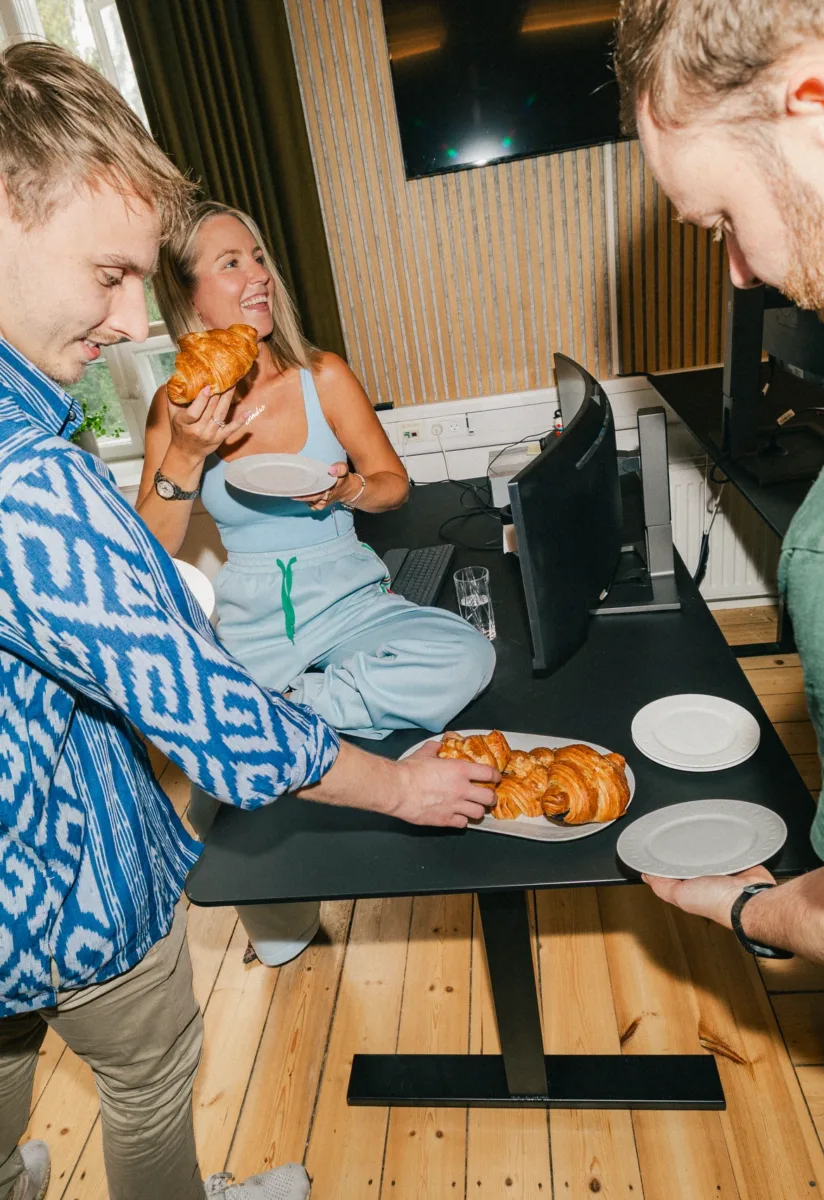 Kollega smiler med en croissant i hånden, mens de andre tager for sig