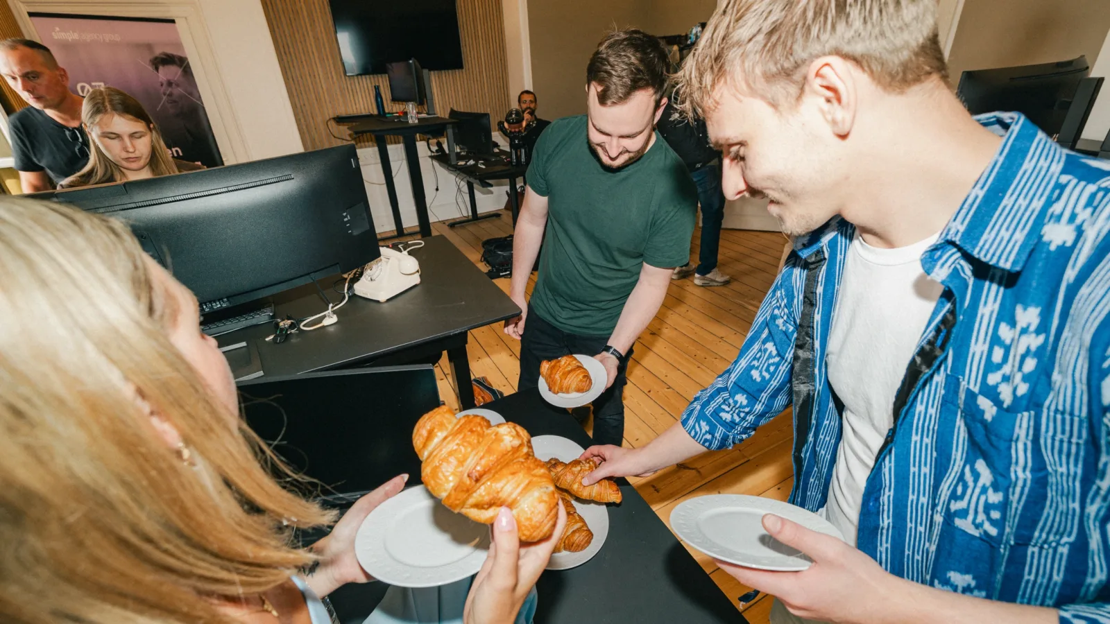 Kolleger samles om et fad croissanter med tallerkener i hænderne