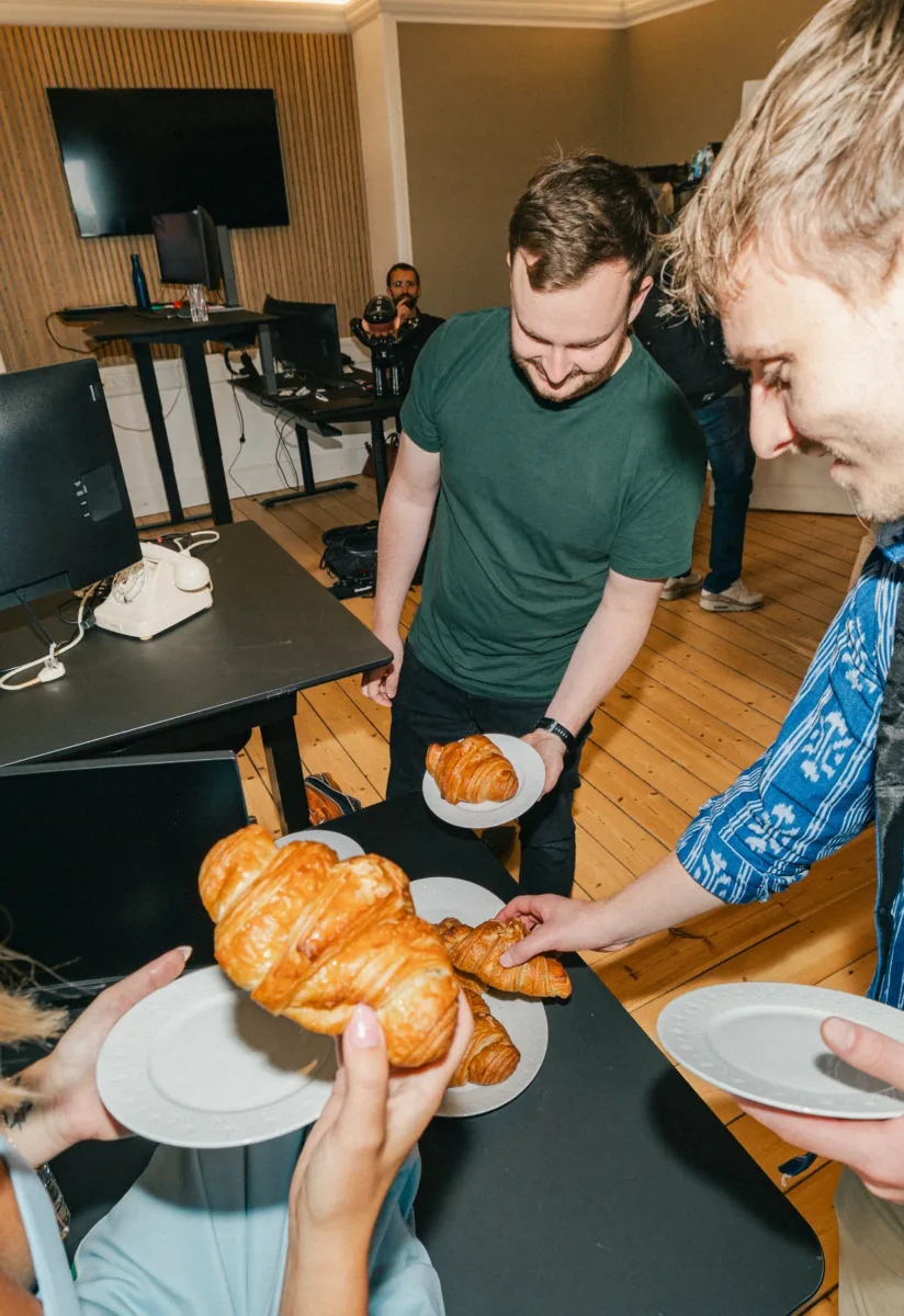 Kolleger samles om et fad croissanter med tallerkener i hænderne