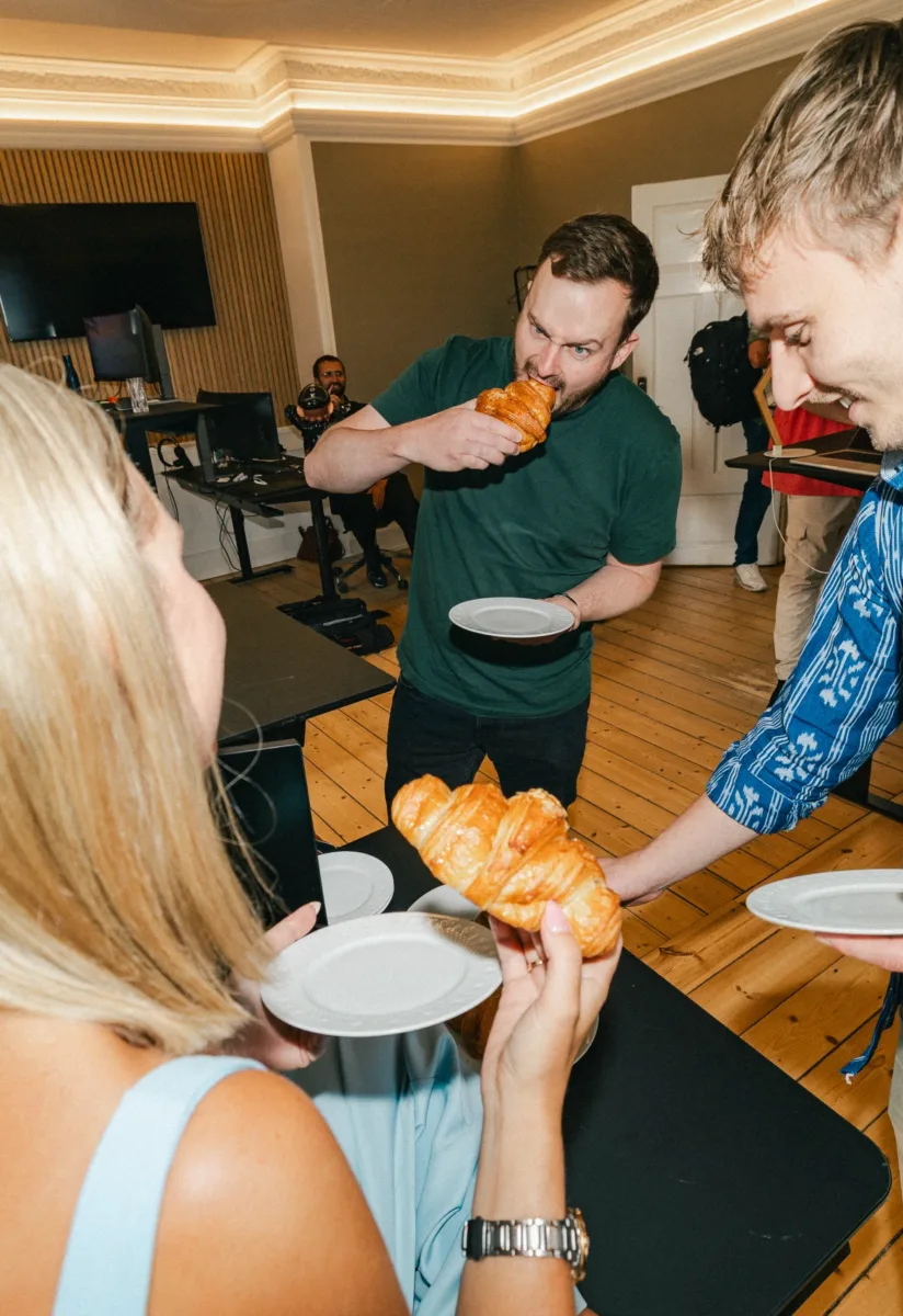 Kollega tager en bid af en croissant, mens de andre står med tallerkener