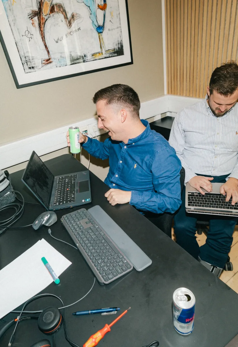 To kolleger arbejder side om side på bærbare computere og griner sammen