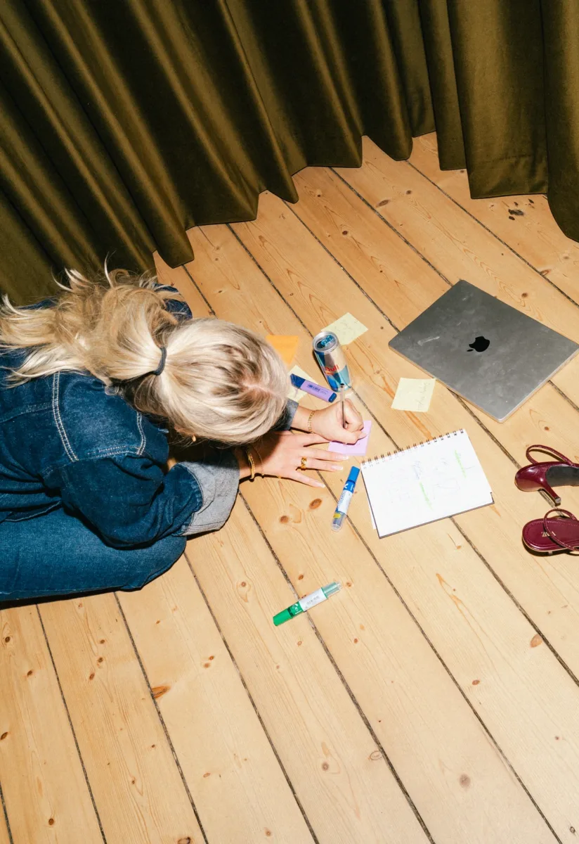 Medarbejder skriver på en post-it på gulvet ved siden af en notesblok med skitser