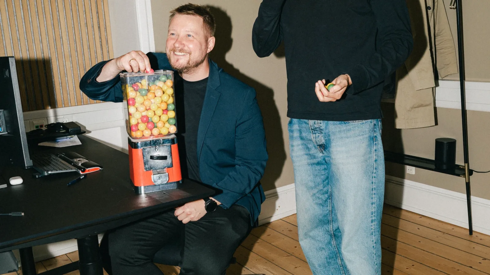 Kolleger smiler med tyggegummi i hånden ved en automat på skrivebordet