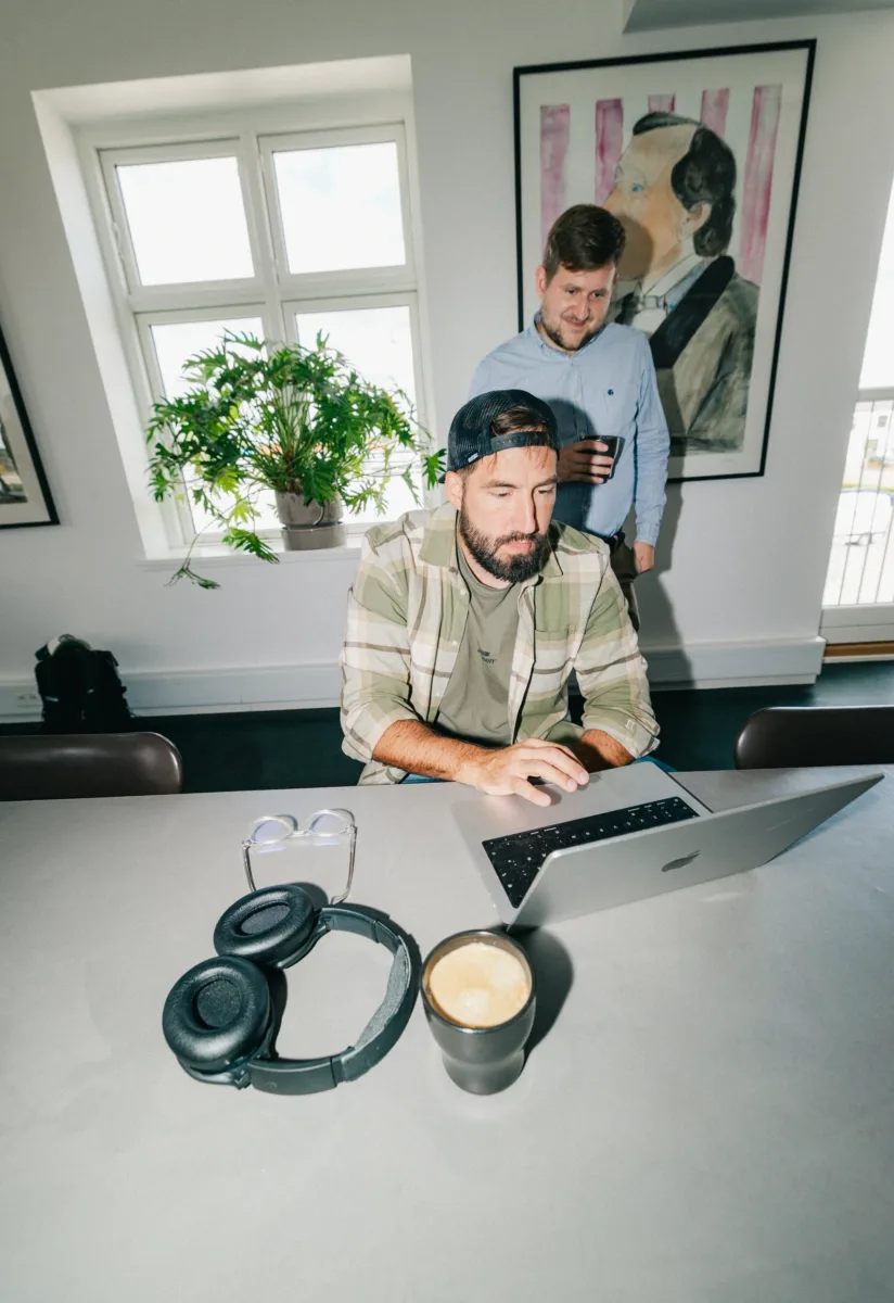 Kollega står med en kop bag en medarbejder, der arbejder på en bærbar computer