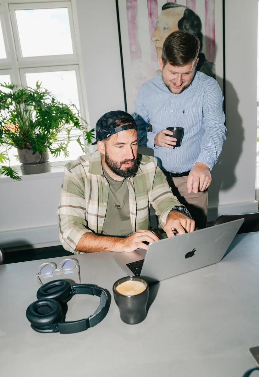 Kollega peger på skærmen på en bærbar computer, mens en anden skriver