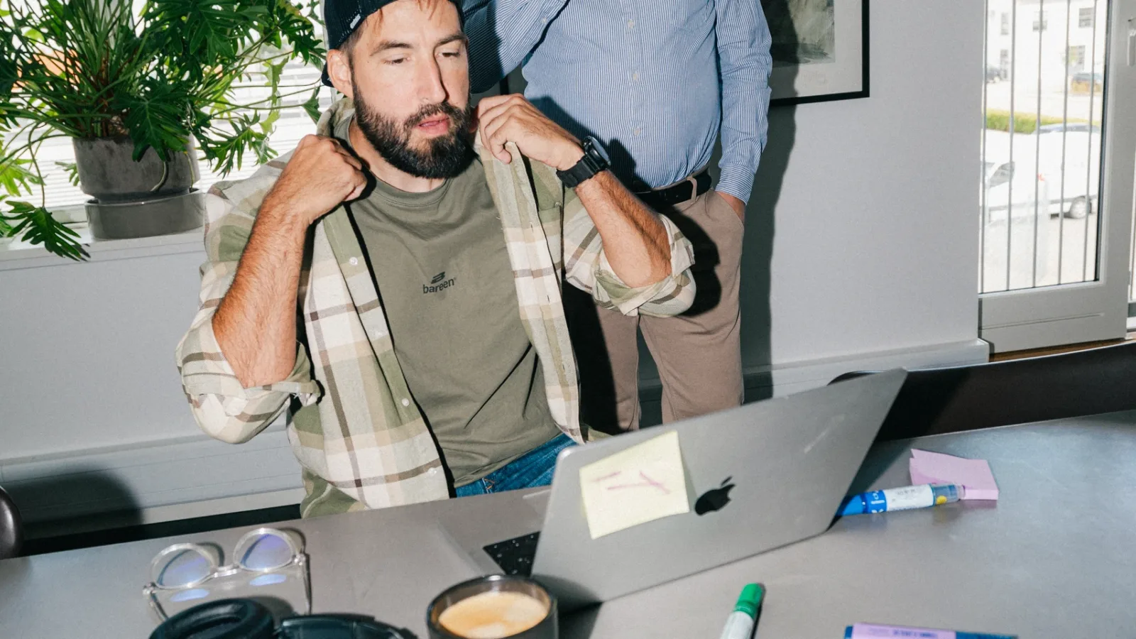 Medarbejder retter sin skjorte, mens en kollega drikker kaffe bagved
