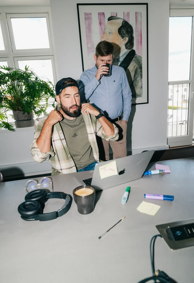 Medarbejder retter sin skjorte, mens en kollega drikker kaffe bagved