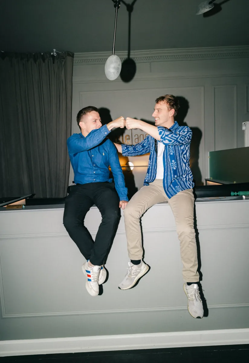 To kolleger griner med næverne mødt i luften siddende på en kant