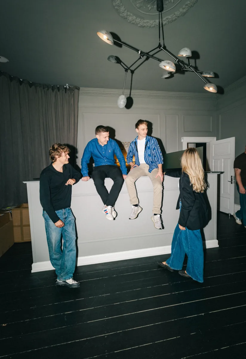 Kolleger samlet omkring en hvid kant og snakker sammen i et mørkt lokale