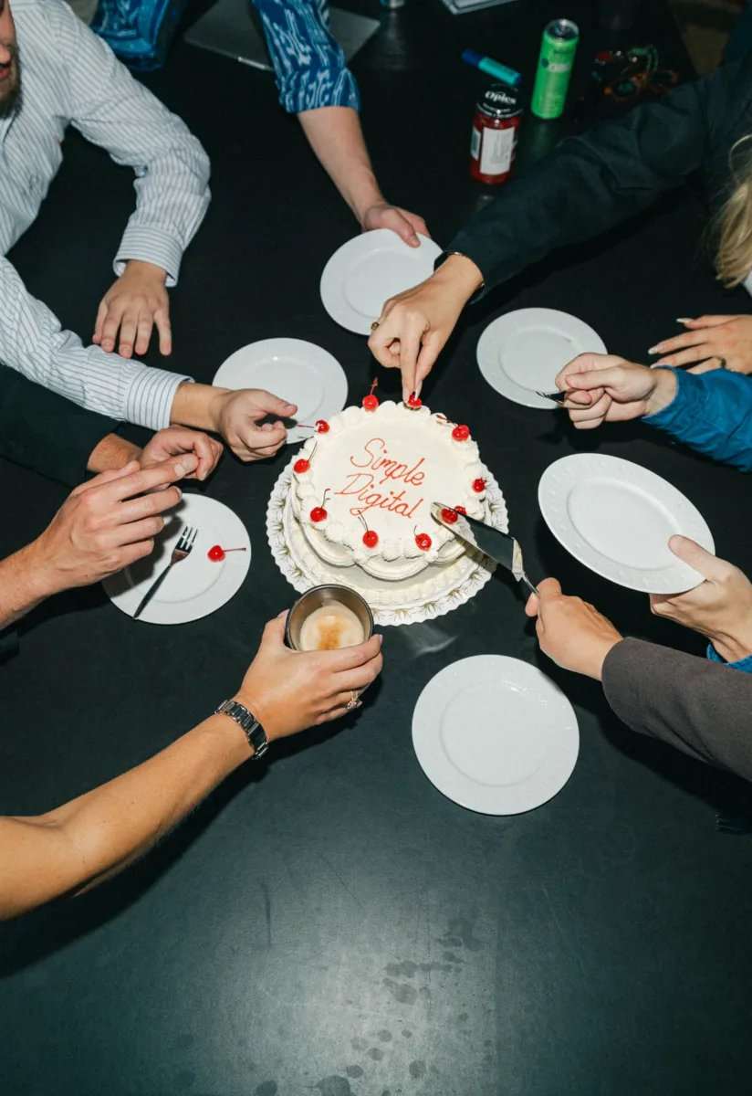 Kolleger samlet om en lagkage med teksten Simple Digital set skråt ovenfra